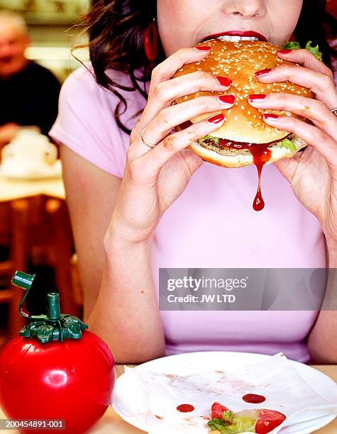 young woman biting into hamburger in diner - tomatenketchup stockfoto's en -beelden