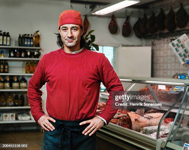 male butcher standing in rural supermarket, hands on hips, portrait - butcher portrait imagens e fotografias de stock