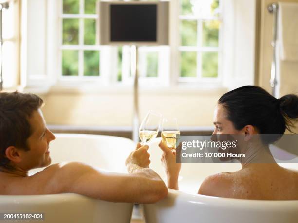 couple in adjacent bubble baths, toasting champagne glasses, rear view - couple bathtub - fotografias e filmes do acervo