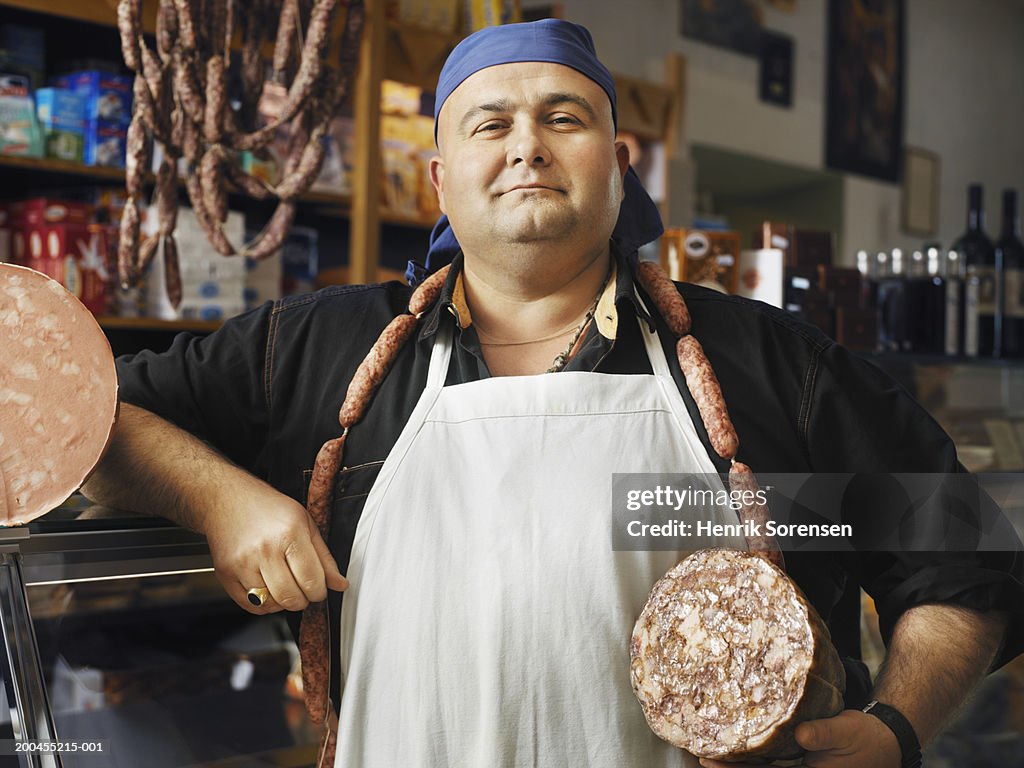 Male butcher holding traditional Italian sausage meats, portrait