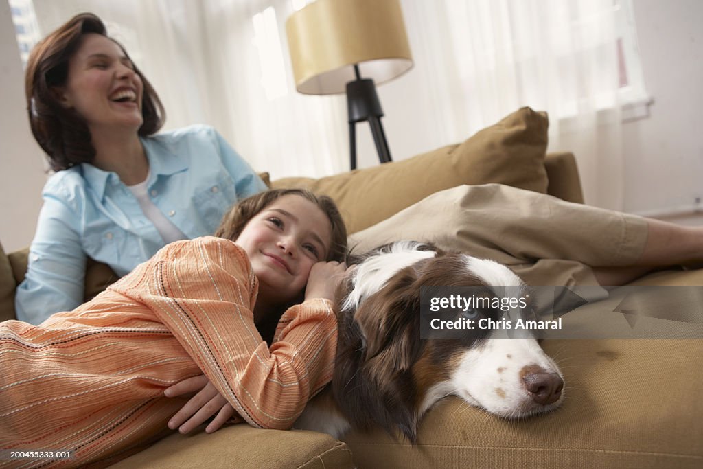 Mother with daughter (8-10) relaxing on sofa with dog, smiling