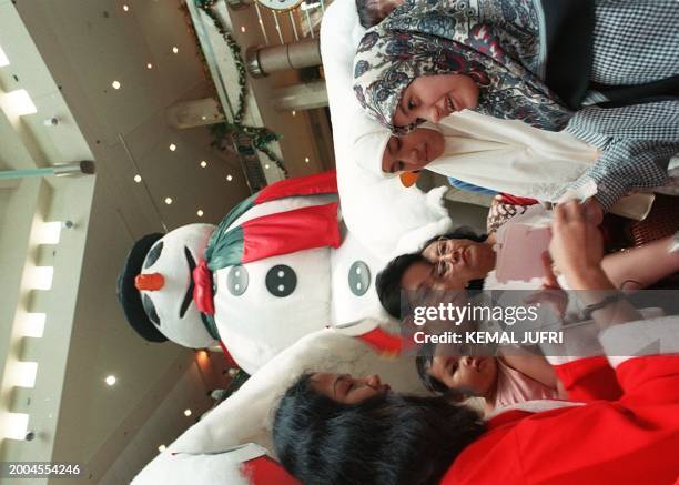 Promotions girl wearing a Santa costume hands out Christmas greeting cards to Moslem women at the entrance of the styrofoam-made ice cave that leads...