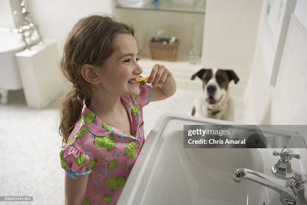 Young girl (8-10) in bathroom brushing her teeth with dog