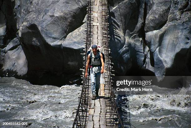 young man crossing rope bridge, elevated view - hangbrug - fotografias e filmes do acervo