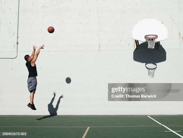 man shooting jump shot on outdoor basketball court, side view - canasta de baloncesto fotografías e imágenes de stock