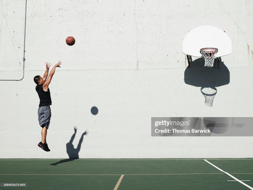 Man shooting jump shot on outdoor basketball court, side view