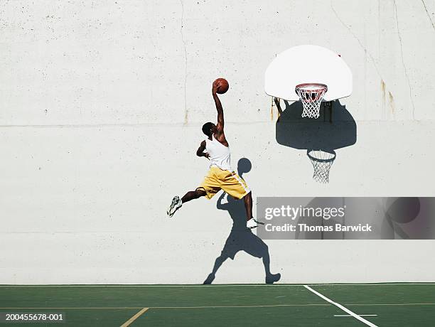 young man shooting at basketball hoop on outdoor court, side view - jump shot ストックフォトと画像