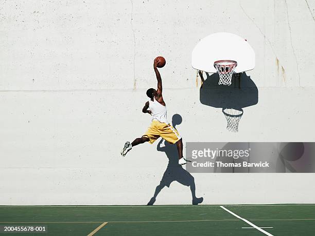 young man shooting at basketball hoop on outdoor court, side view - arremesso de jump no basquetebol - fotografias e filmes do acervo