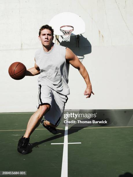 young man dribbling basketball on outdoor basketball court - dribbling sport fotografías e imágenes de stock