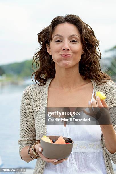 young woman eating fruit on dock, smiling, portrait, close-up - vollgestopft stock-fotos und bilder
