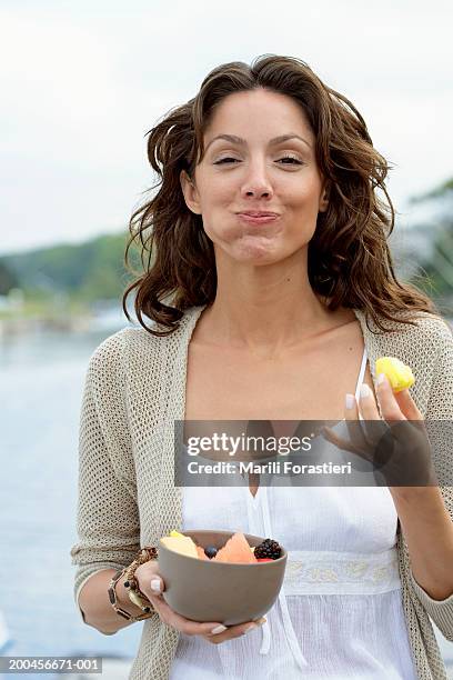 young woman eating fruit on dock, smiling, portrait, close-up - woman mouth stock-fotos und bilder