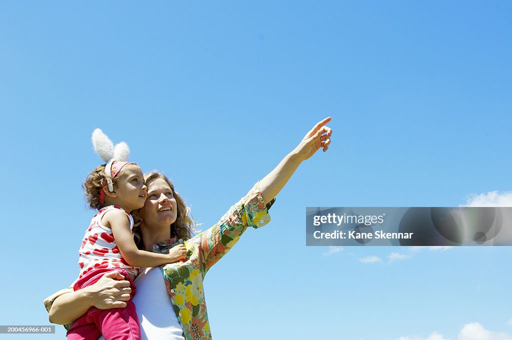 Mother holding daughter (3-5) wearing bunny ears, pointing upwards