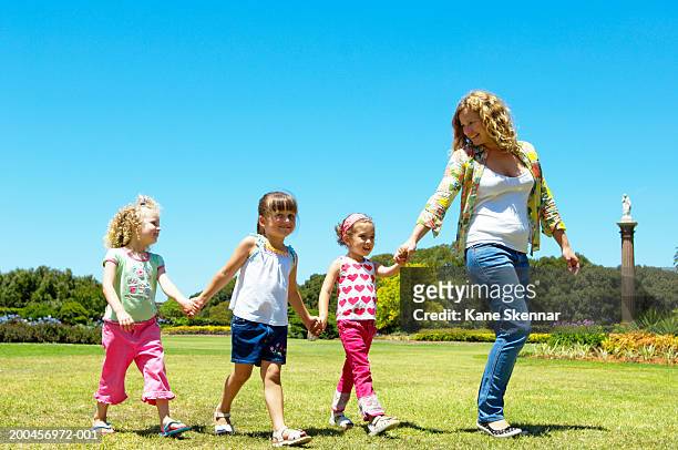 woman and three girls (3-5) holding hands, walking through park - centennial park stock-fotos und bilder