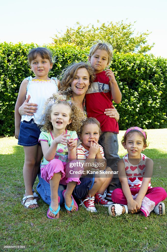 Woman with group of children (3-6) in park, smiling, portrait