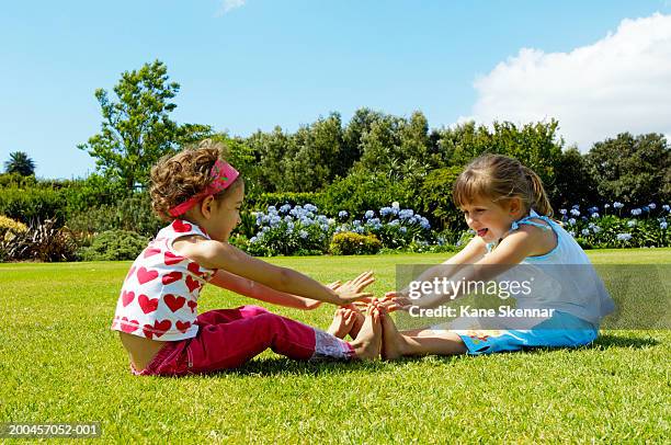 two girls (3-5) sitting in park, reaching to touch toes - toe - fotografias e filmes do acervo