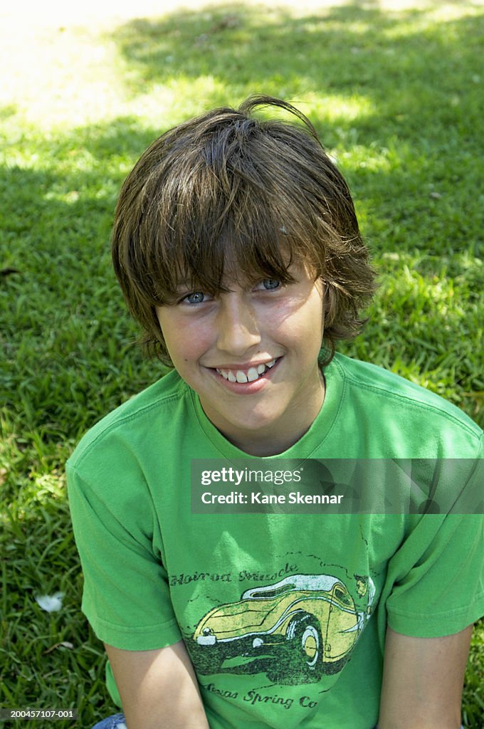 Boy (11-13) sitting on grass, smiling, portrait