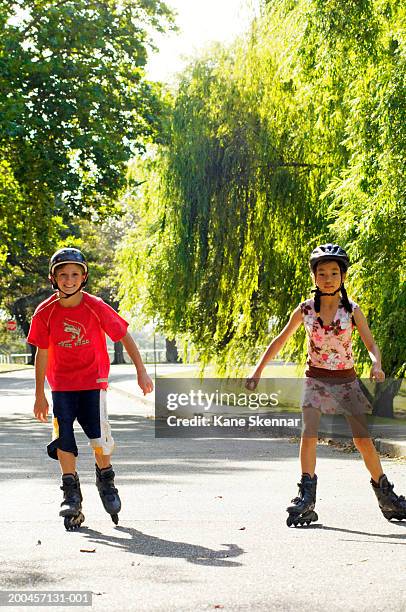 boy and girl (10-12) inline skating in park,wearing protective helmets - rolschaatsen schaats stockfoto's en -beelden
