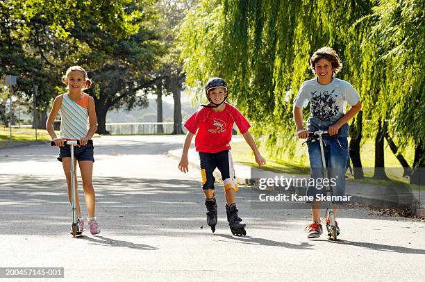 two boys and girl (9-12)in park,riding scooters and one inline skating - girl roller skates stock pictures, royalty-free photos & images