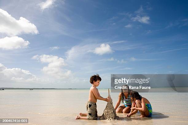 three kids (7-10) building sand castle on beach - kind sandburg stock-fotos und bilder