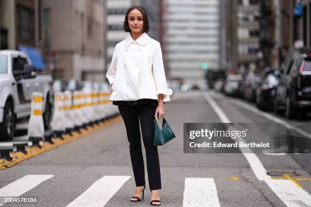 Guest wears a white flared double breasted white jacket in oversized , a green leather bag, black suit pants , high heels shoes , outside Altuzarra,...