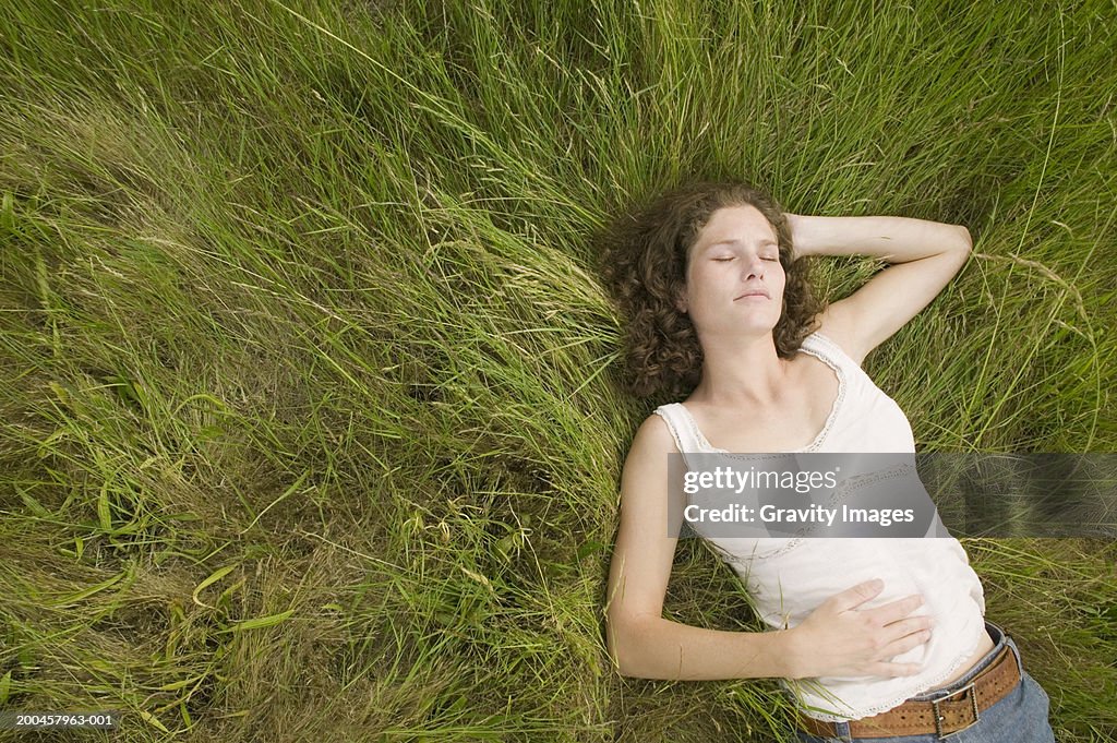 Young woman lying on grass, eyes closed, overhead view