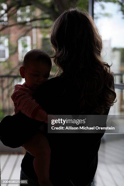 mother holding baby boy (6-9 months) at door, rear view, silhouette - woman walking out door silhouette stock pictures, royalty-free photos & images