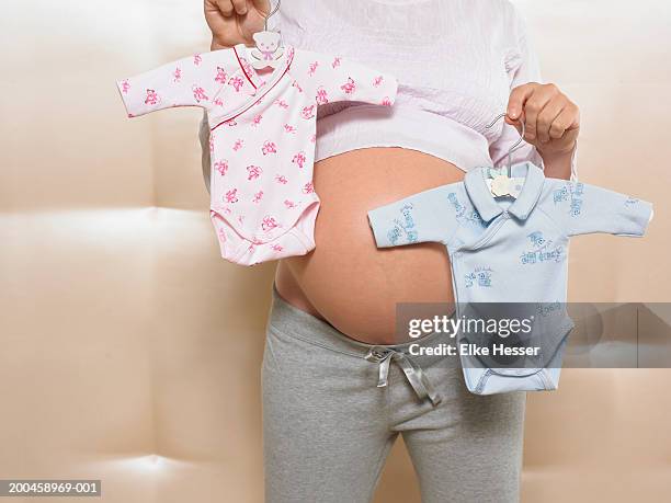 pregnant woman holding pink and blue babygrows, mid section - strampelanzug stock-fotos und bilder