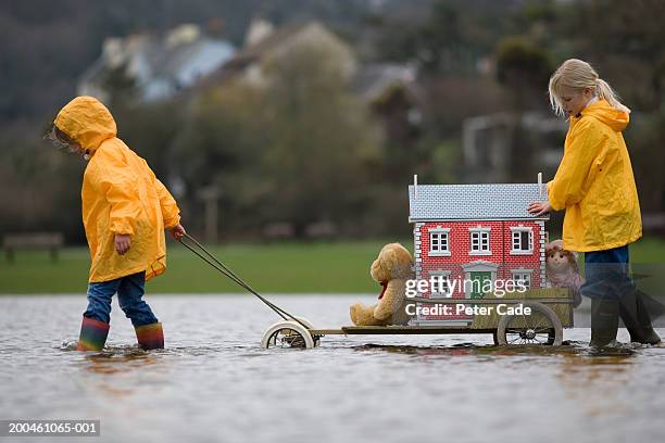 two girls (7-9) moving doll house on cart through water, side view - girl side view stock-fotos und bilder