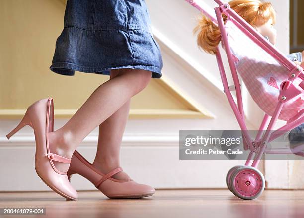 girl (3-5) wearing adult shoes, pushing doll in pram, low section - bambola giocattolo foto e immagini stock