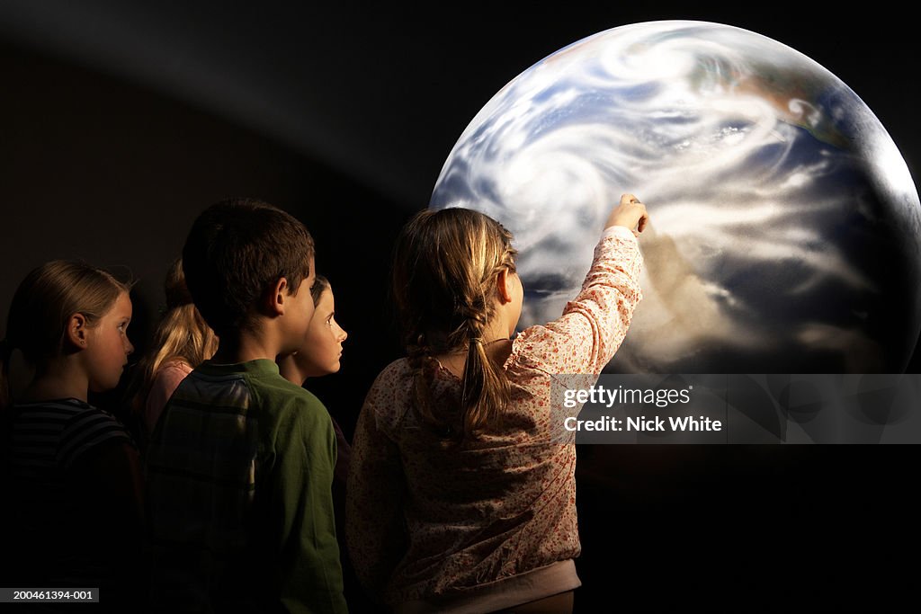 Group of children (8-10) looking at model of Earth, rear view