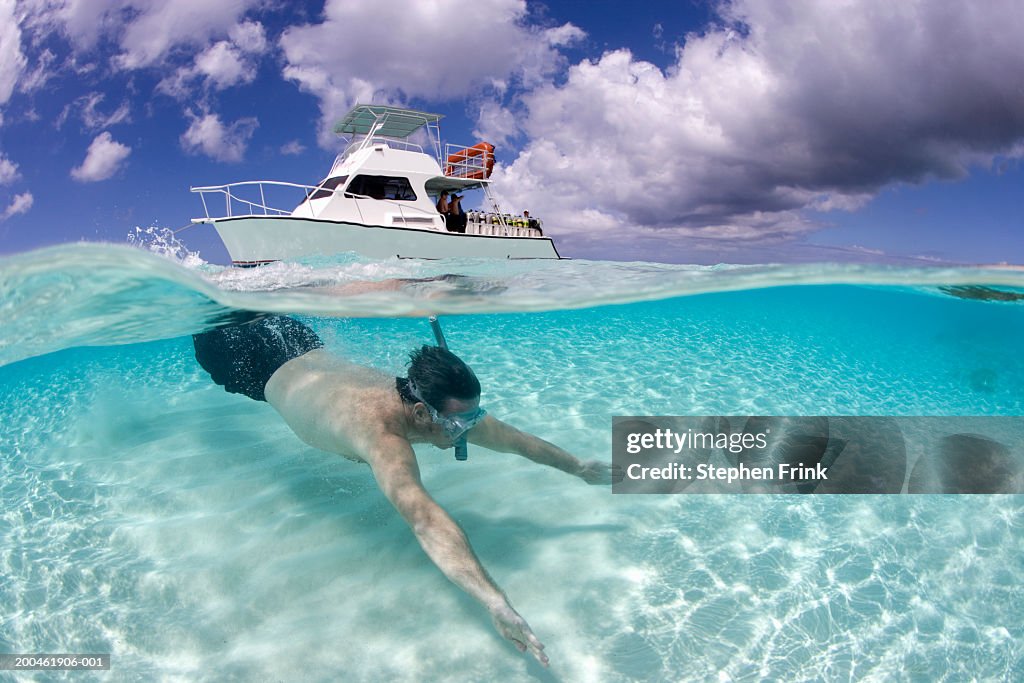 Man snorkeling, dive boat in background, surface view