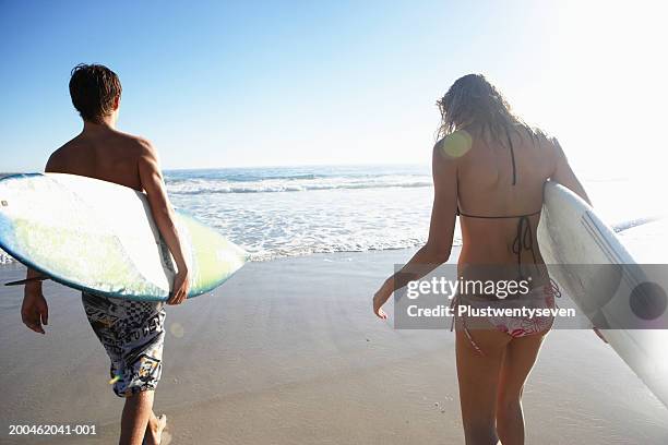 teenage boy (14-16) and young woman carrying surfboards on beach - camps bay stock pictures, royalty-free photos & images