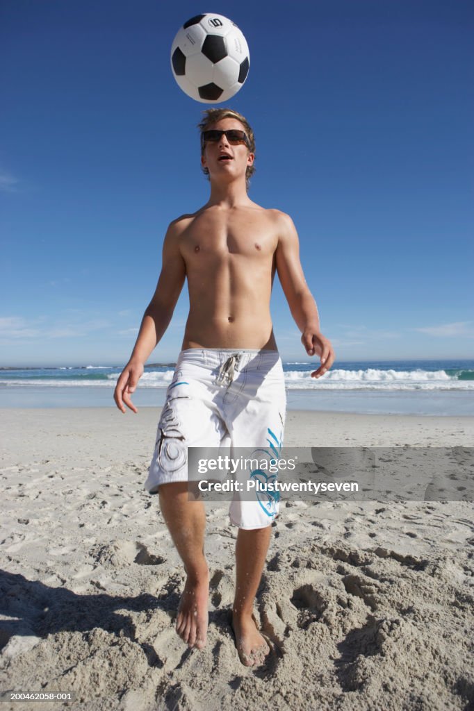 Teenage boy (15-17) practicing soccer skills on beach