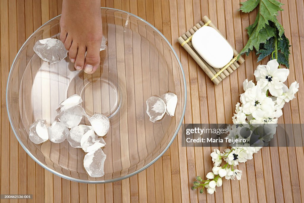 Young woman placing foot in bowl of water and petals, low section
