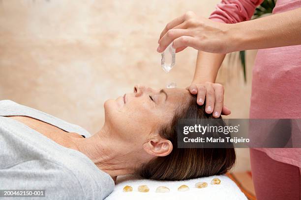 mature woman receiving crystal healing treatment, eyes closed - healing crystals stock pictures, royalty-free photos & images