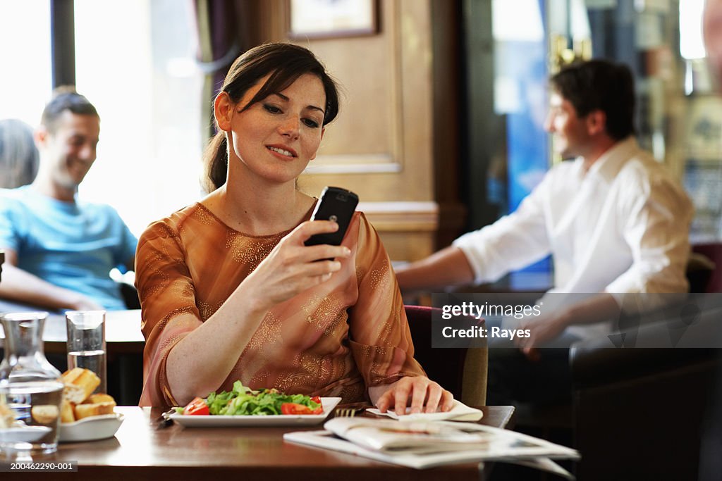 Woman sitting at table in bar, looking at mobile phone, smiling