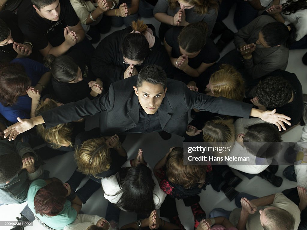 Group of young people praying towards man in center, view from above