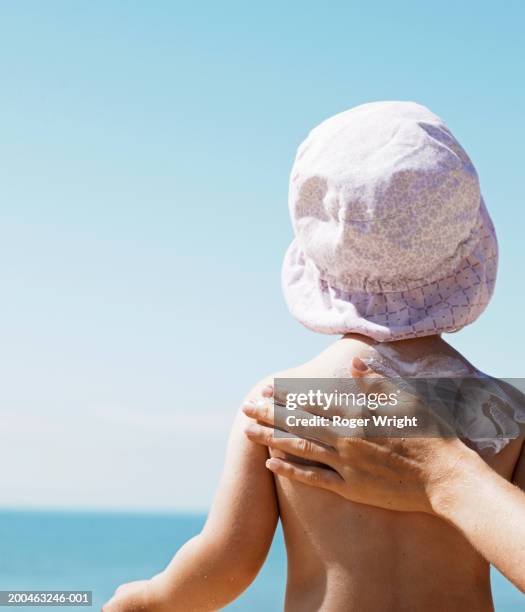 mother rubbing suncream on daughter (1-3) on beach, rear view - sunscreen imagens e fotografias de stock