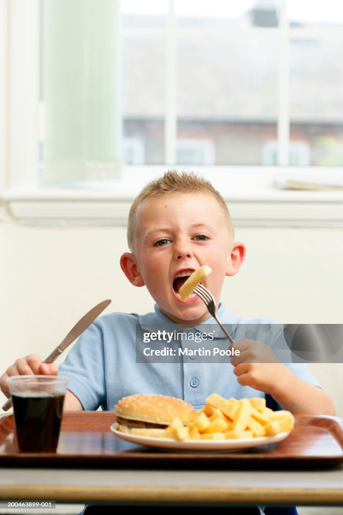 Boy (5-7) eating burger and chips, portrait