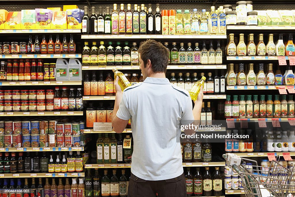 Young man in supermarket comparing bottles of oil, rear view, close-up