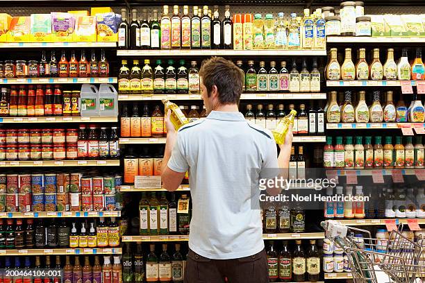 young man in supermarket comparing bottles of oil, rear view, close-up - consumerism stock pictures, royalty-free photos & images