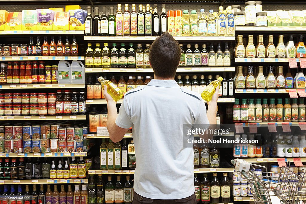 Young man looking at bottles of oil in market, rear view, close-up