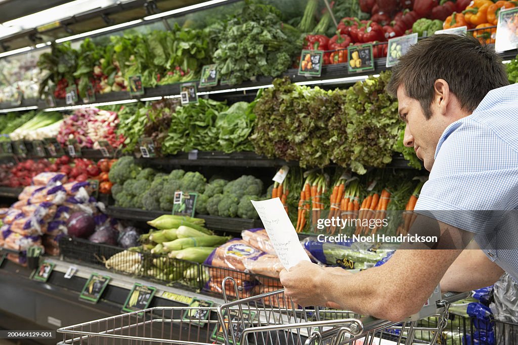 Young man reading shopping list in produce aisle, side view, close-up