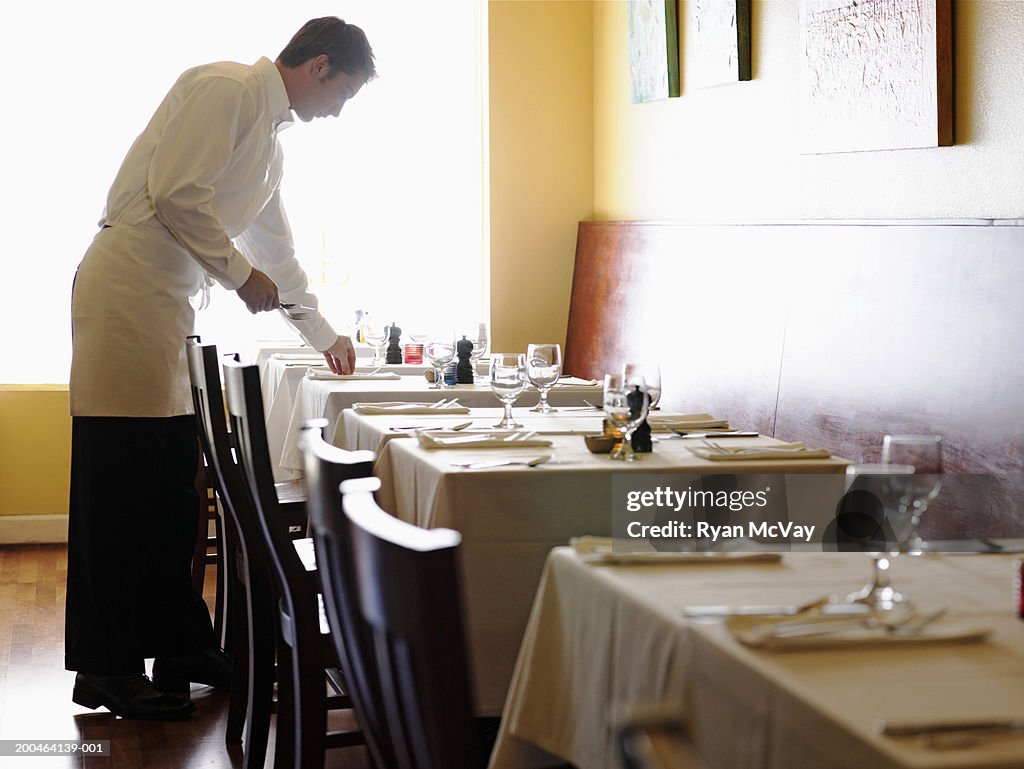 Young man setting tables in restaurant, side view