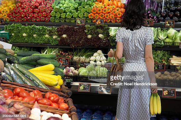 woman holding bananas in produce aisle of supermarket, rear view - secção de frutas e legumes imagens e fotografias de stock