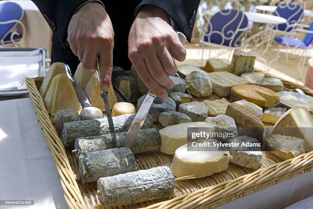 Person cutting slice of cheese on cheese plate