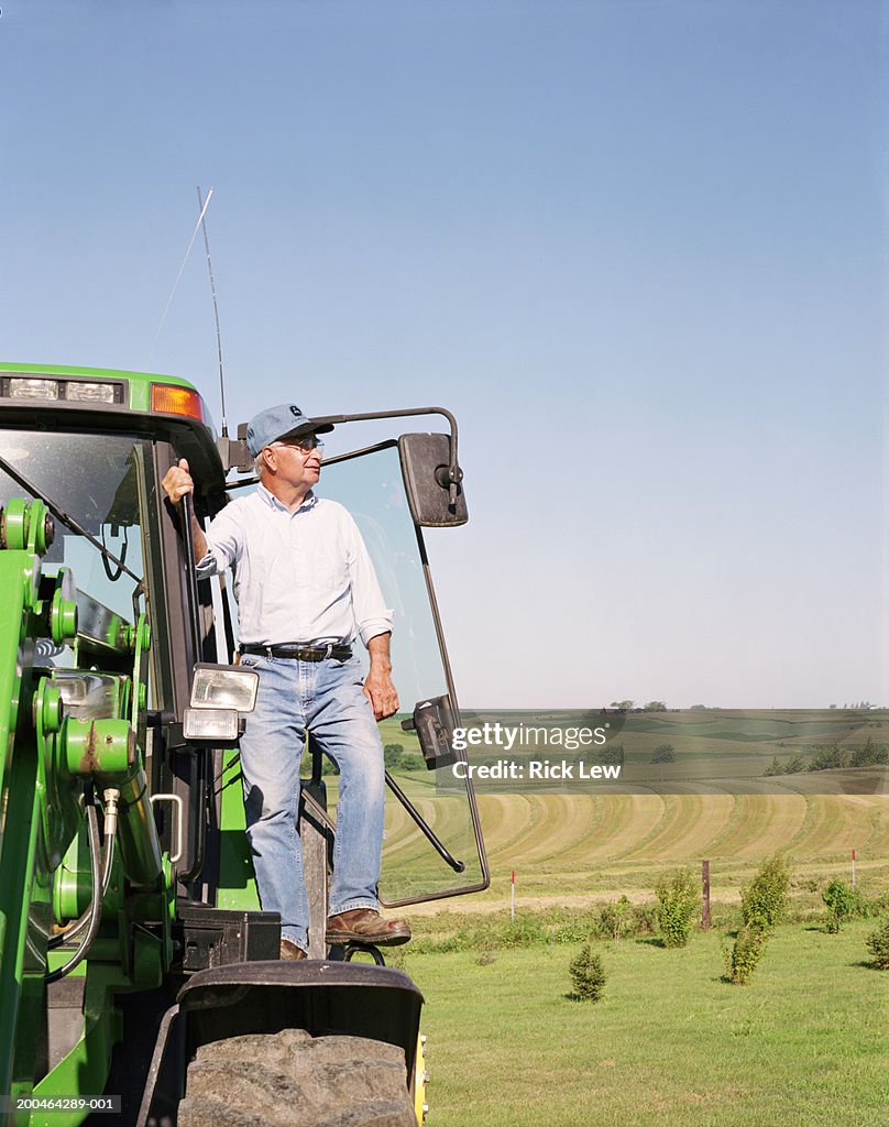 Farmer standing on wheel of tractor
