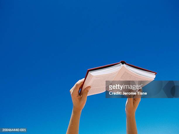 young woman holding book up in air, low angle view - reading stock-fotos und bilder