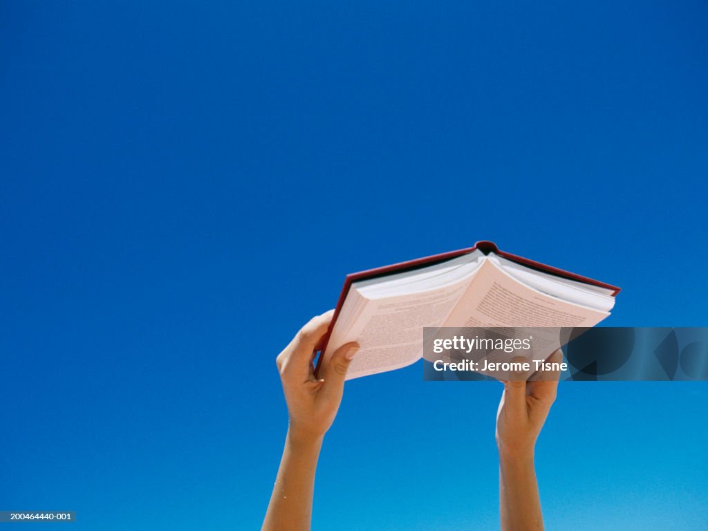 Young woman holding book up in air, low angle view
