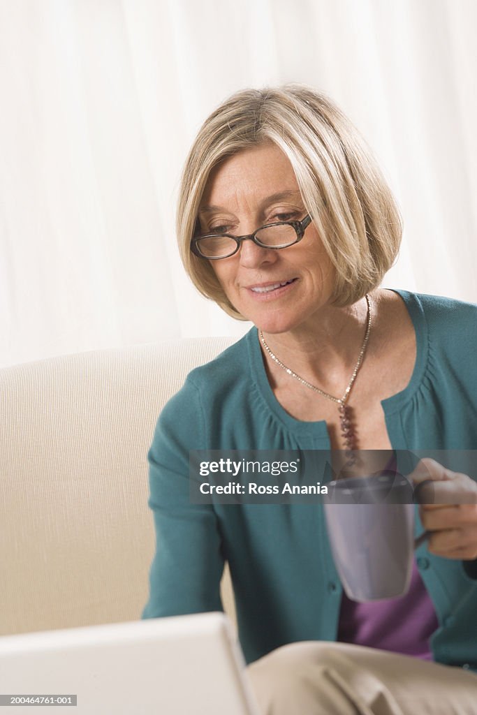 Mature woman working on laptop, holding mug, close-up